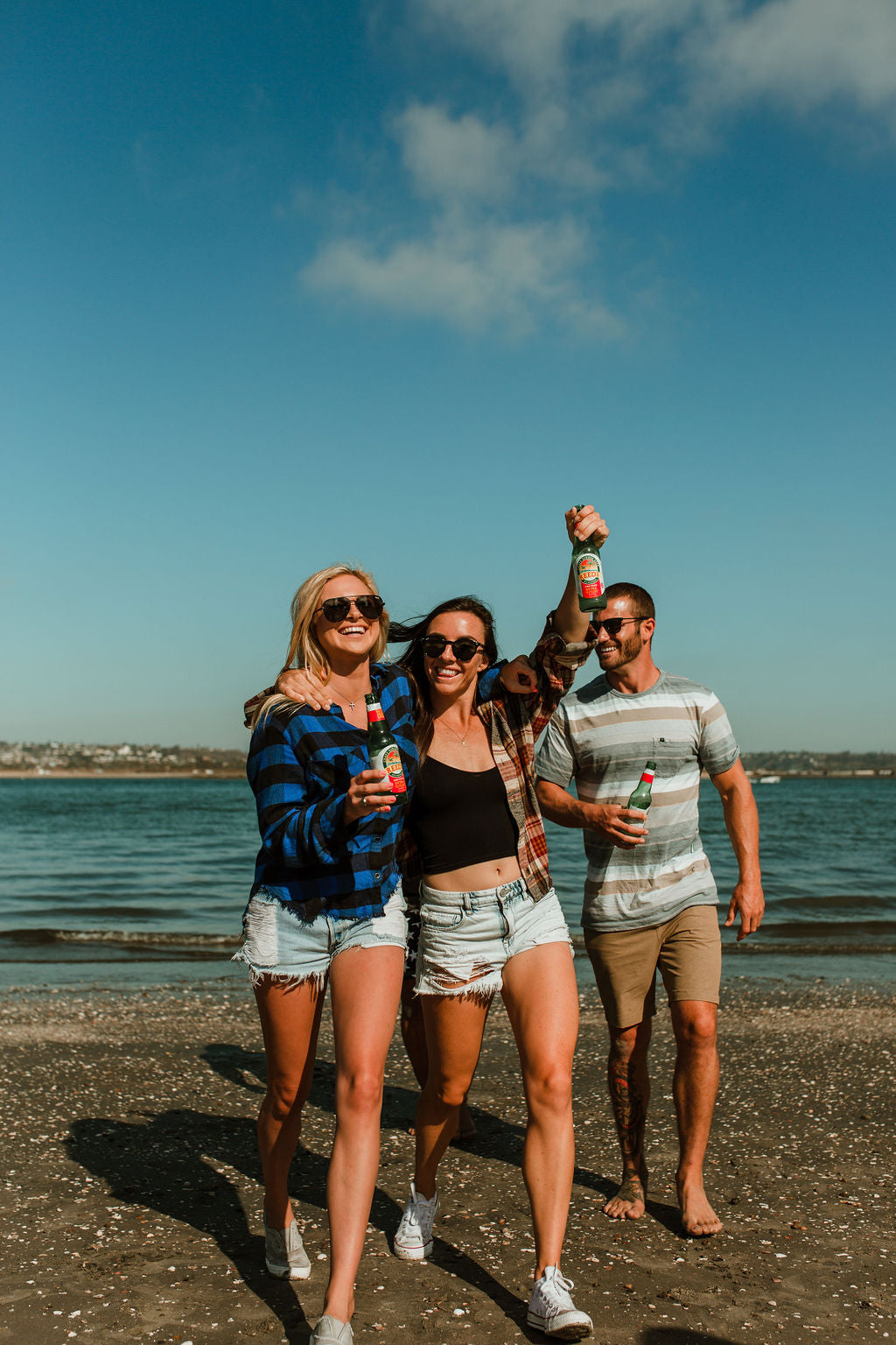 Two girls and a guy on the beach walking and drinking Reed's Zero Sugar Extra Ginger Beer.
