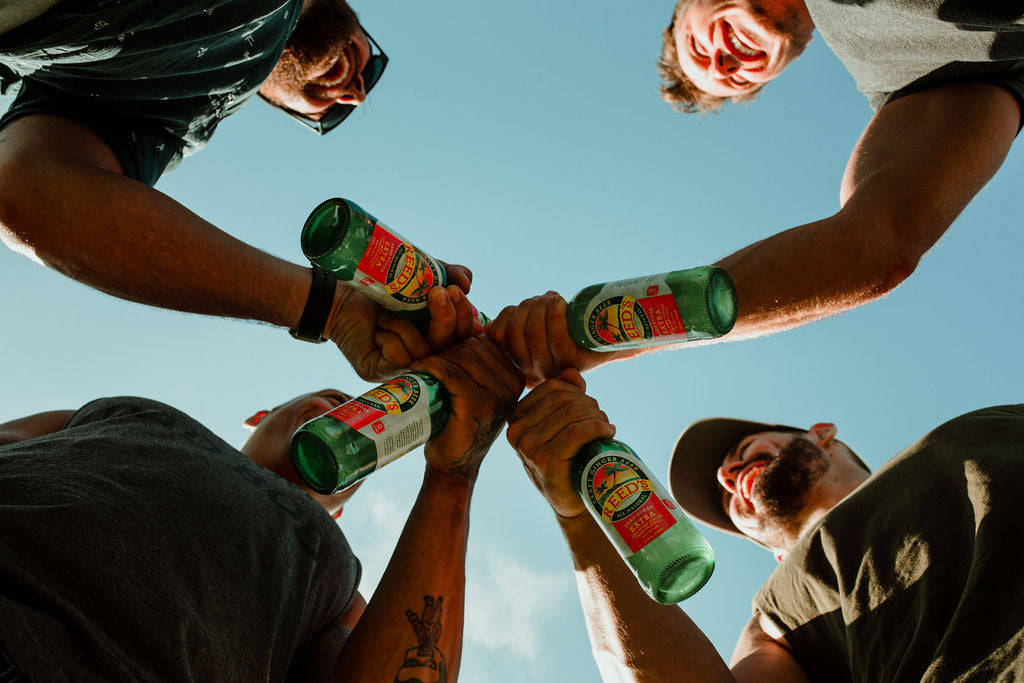 Four guys holding glass bottles of Reed's Zero Sugar Extra Ginger Beer.