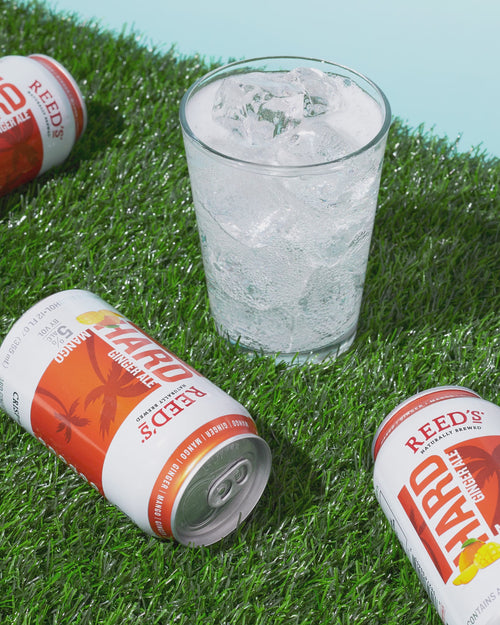 Reed's Hard Ginger Ale rolling on the grass next to a glass of clear liquid.