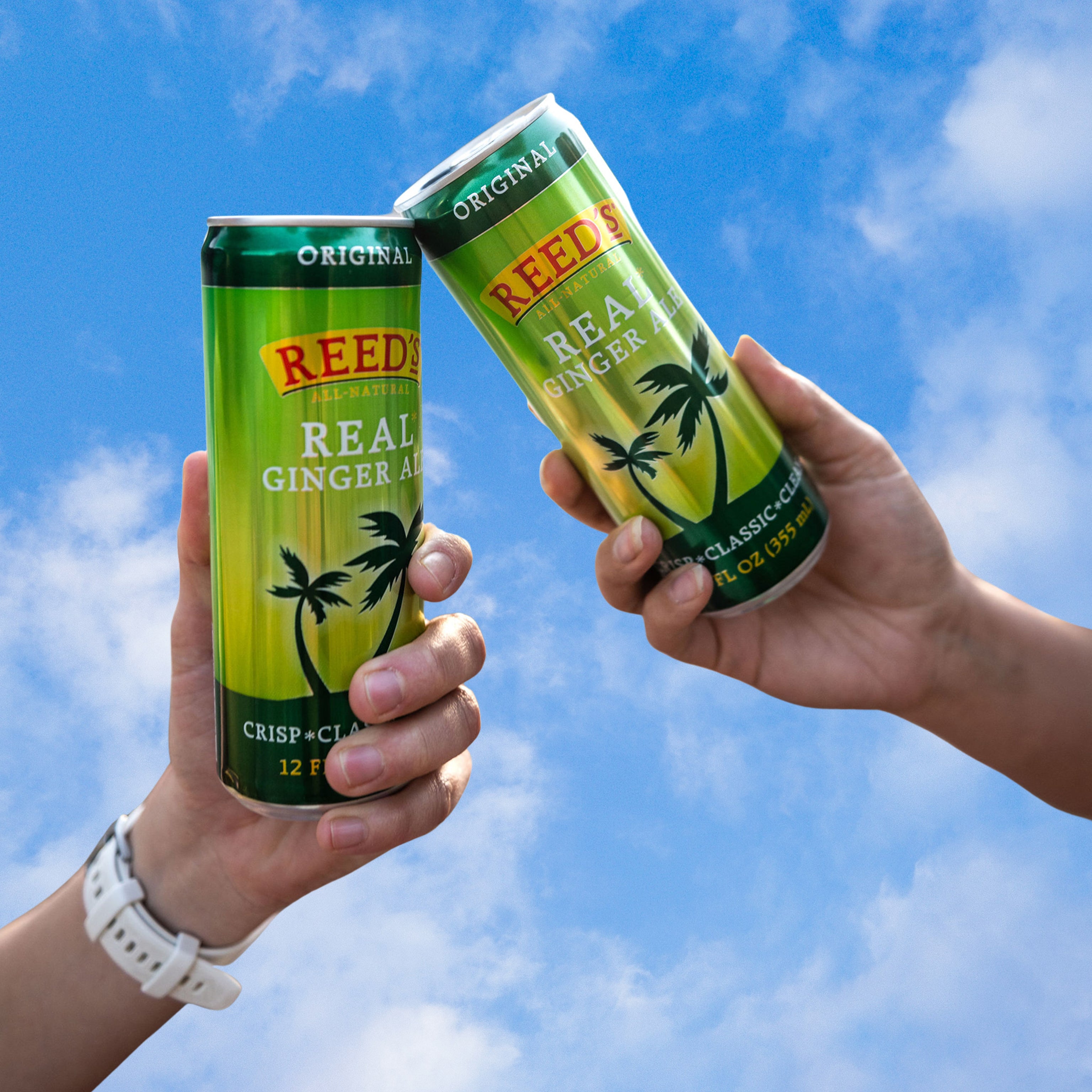 People holding Reed's Real Ginger Ale slim cans in front of a cloudy background.